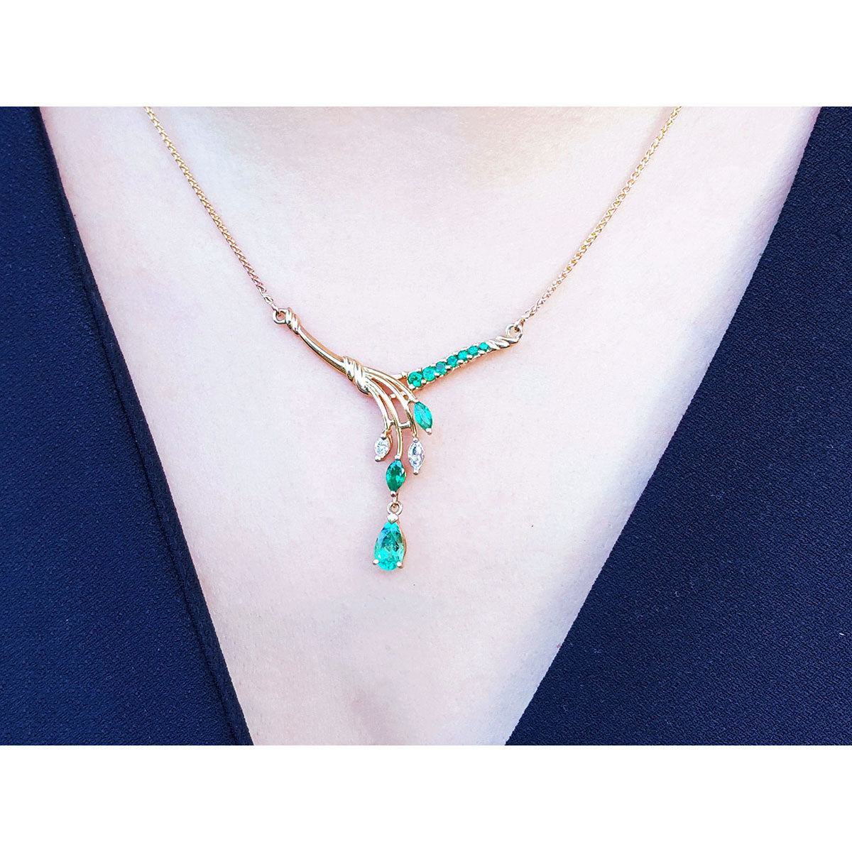 A close view of a yellow gold necklace with natural emeralds gemstones and diamonds worn by a woman