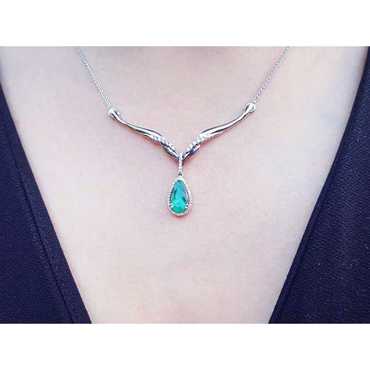 A close view of a necklace with a emerald stone teardrop pendant on a person wearing a dark top.