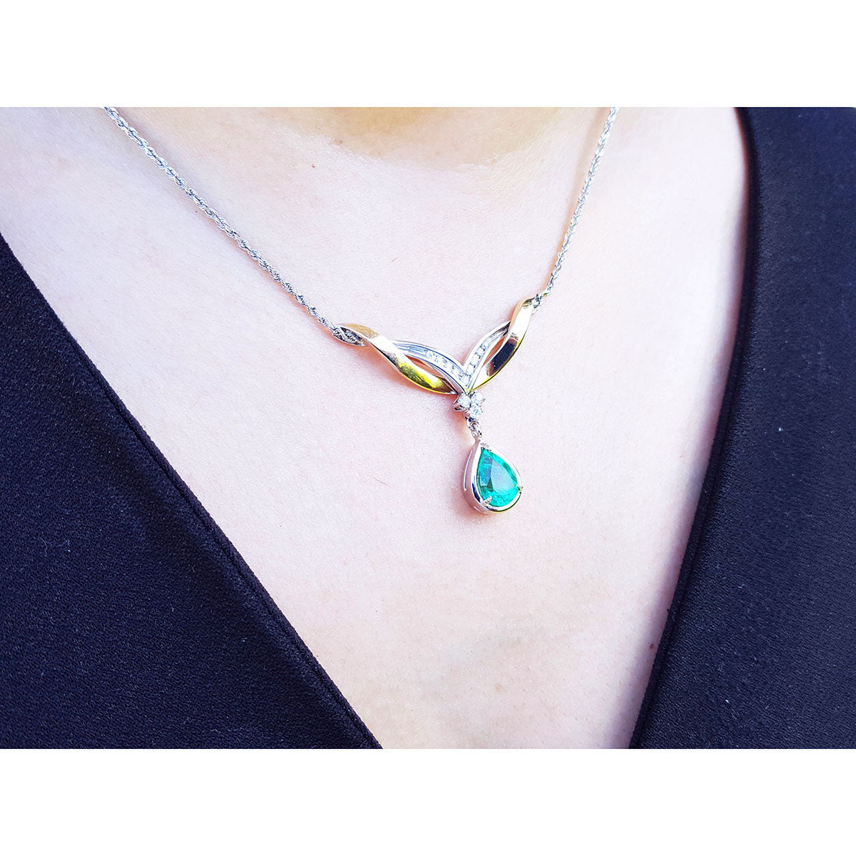 A close view of a necklace with a dangling teardrop-shaped emerald pendant on a woman wearing a black top.