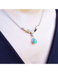 A close view of a necklace with a dangling teardrop-shaped emerald pendant on a woman wearing a black top.