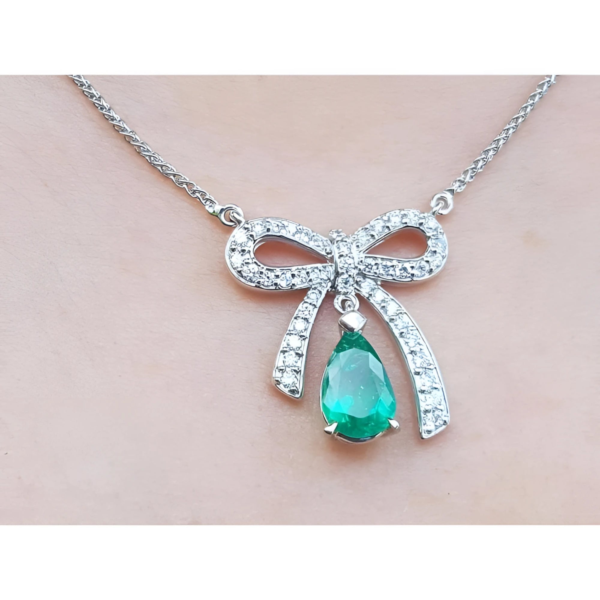 18K white gold bow-tie necklace with a pear-shaped deep green emerald pendant.
