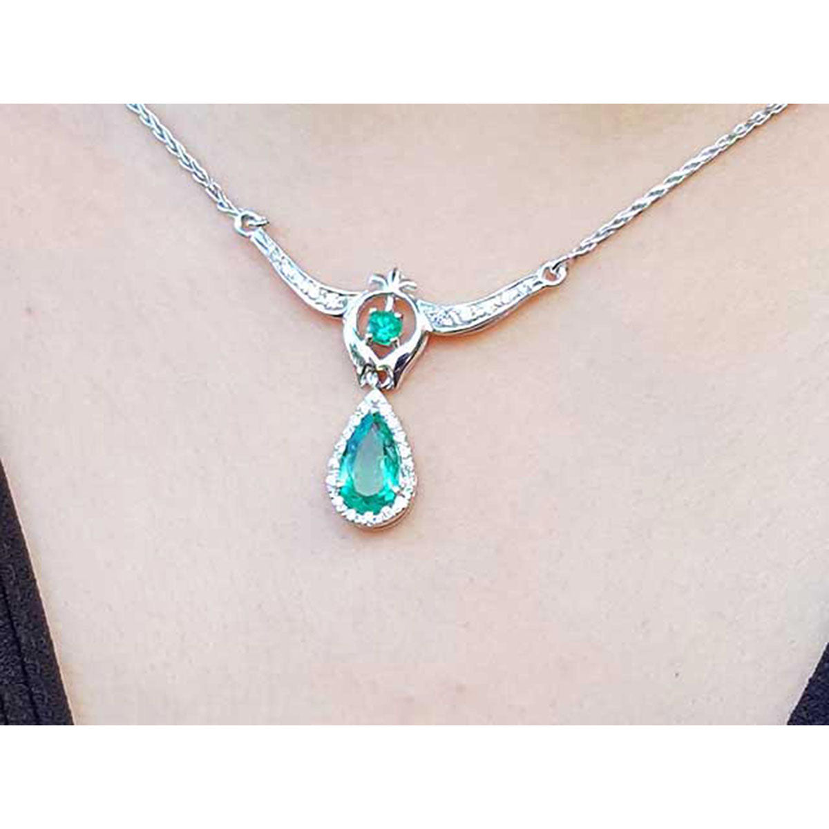 On a close view a white gold necklace with a teardrop-shaped emerald pendant on a plain background