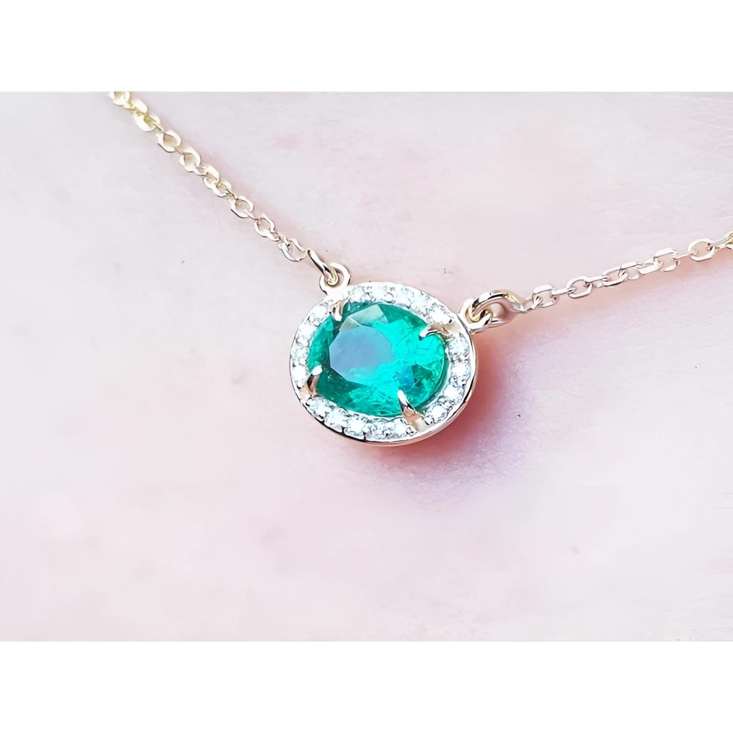 0.90 carat oval Muzo emerald necklace with diamond halo on a 14K yellow gold chain.