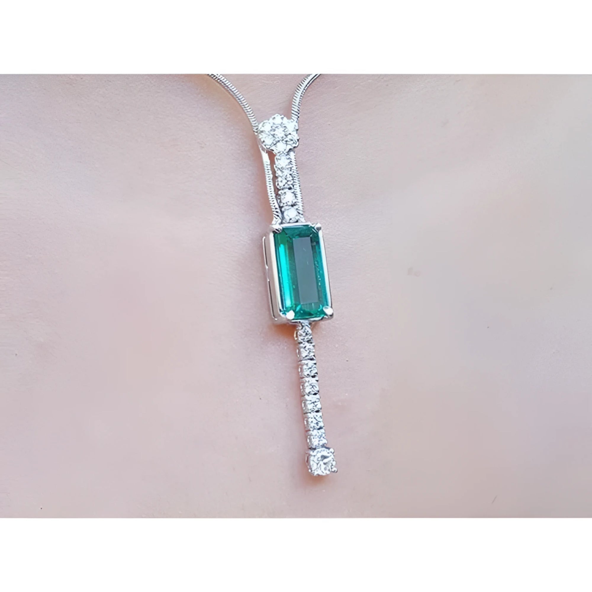 White gold women's necklace with a rectangular Colombian emerald and diamond accents, worn on a neck.