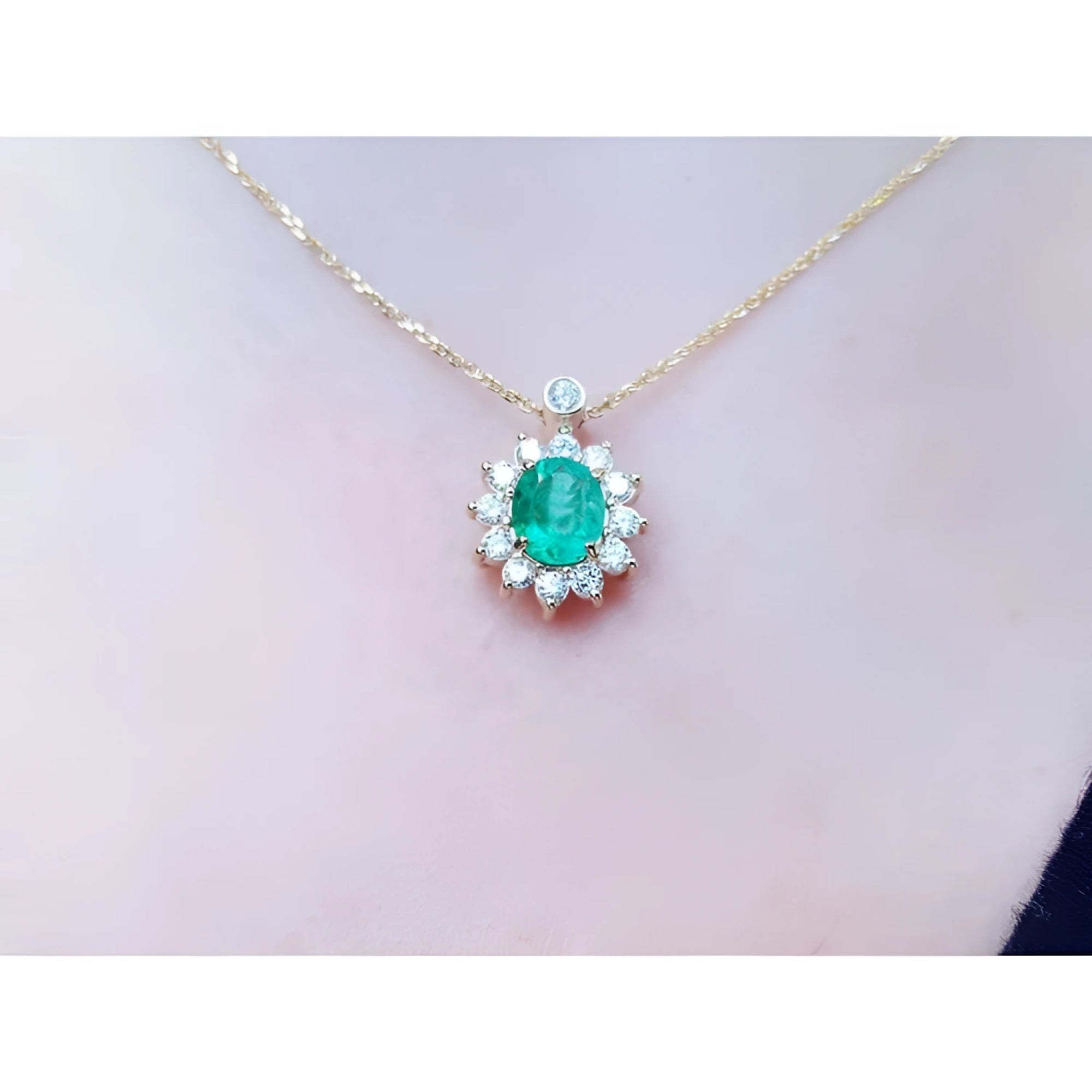 Oval cut 1.11 ct. emerald and natural diamond cluster necklace on a 14K yellow gold chain.