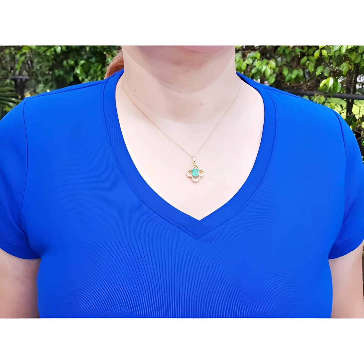 14K gold clover pendant with a square emerald and diamonds, worn on a woman in a blue shirt.
