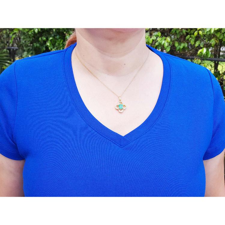 14K gold clover pendant with a square emerald and diamonds, worn on a woman in a blue shirt.