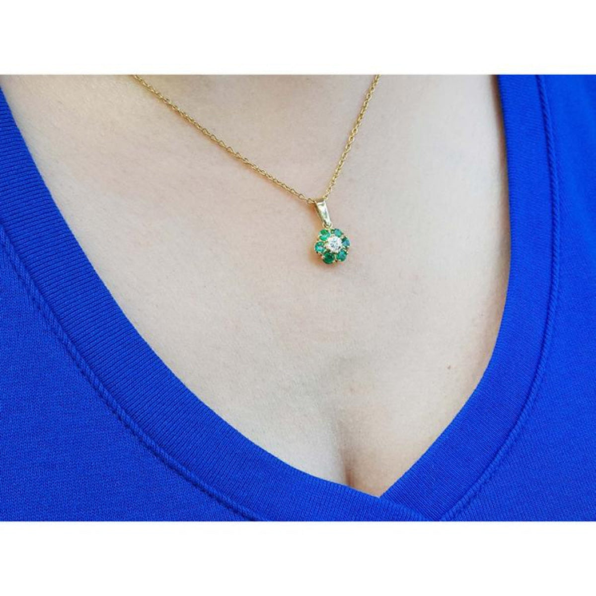 18K yellow gold cluster pendant with deep green emeralds and a center diamond on a woman's neck.