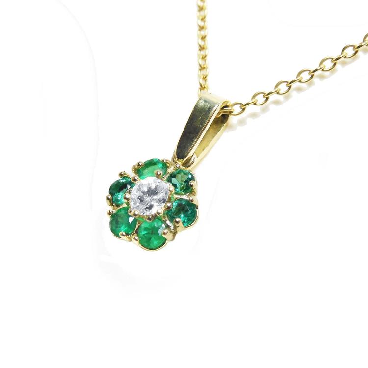 Six rounds cut natural colombian emeralds surrounding a diamond forming a cluster pendant necklace.