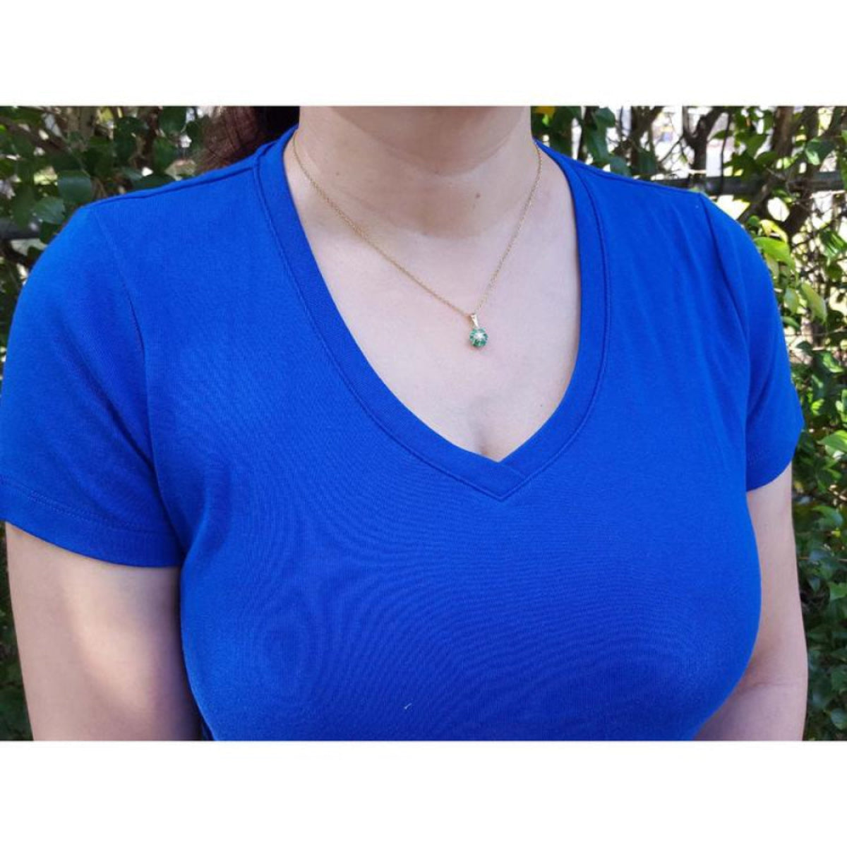 18K yellow gold cluster emerald and diamond pendant necklace on a woman in a blue shirt.