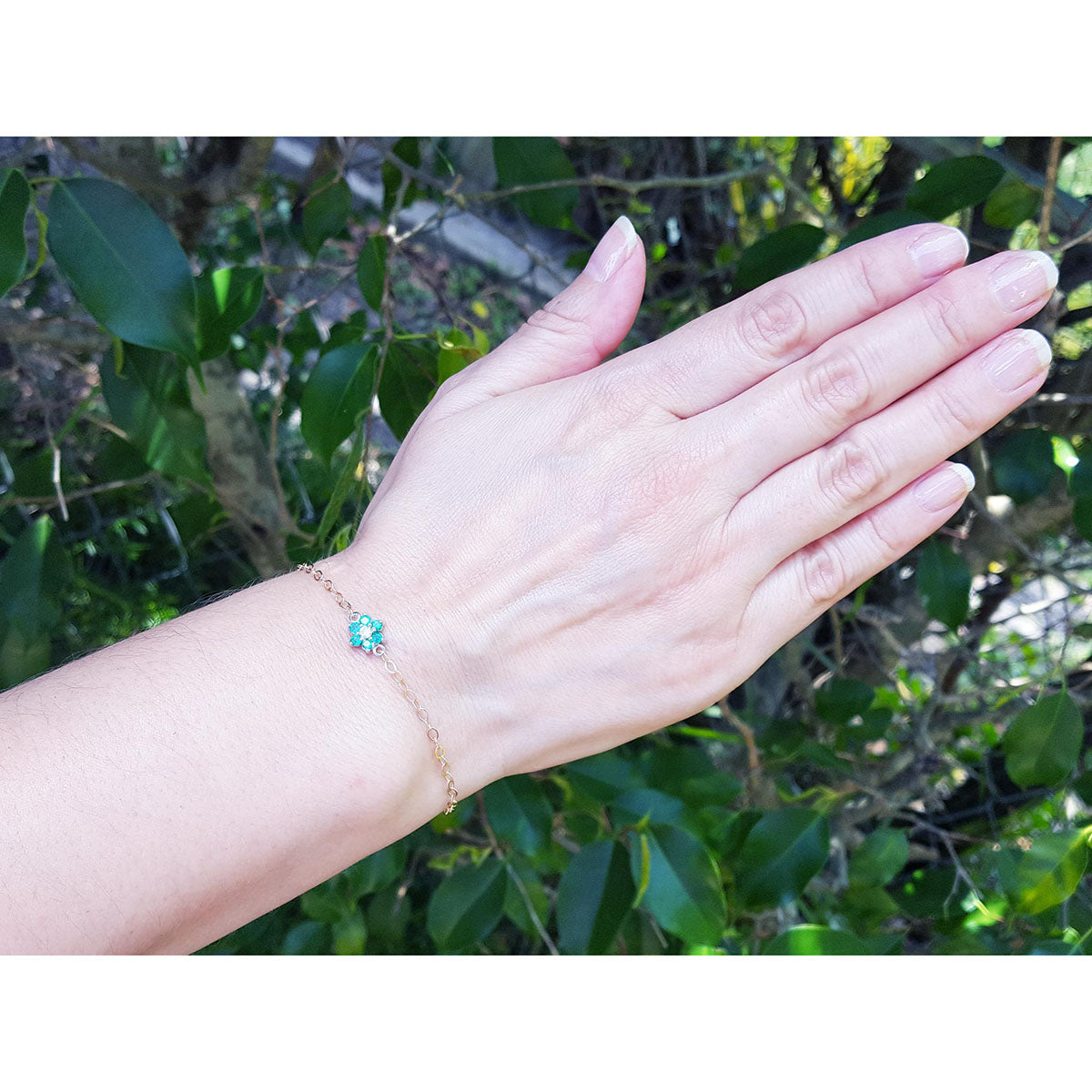 Hand wearing a bracelet with a emerald and diamond cluster against a natural background.
