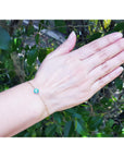 Hand wearing a bracelet with a emerald and diamond cluster against a natural background.