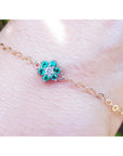 Gold bracelet with a emerald flower-shaped clasp on a wrist against a blurred natural background.