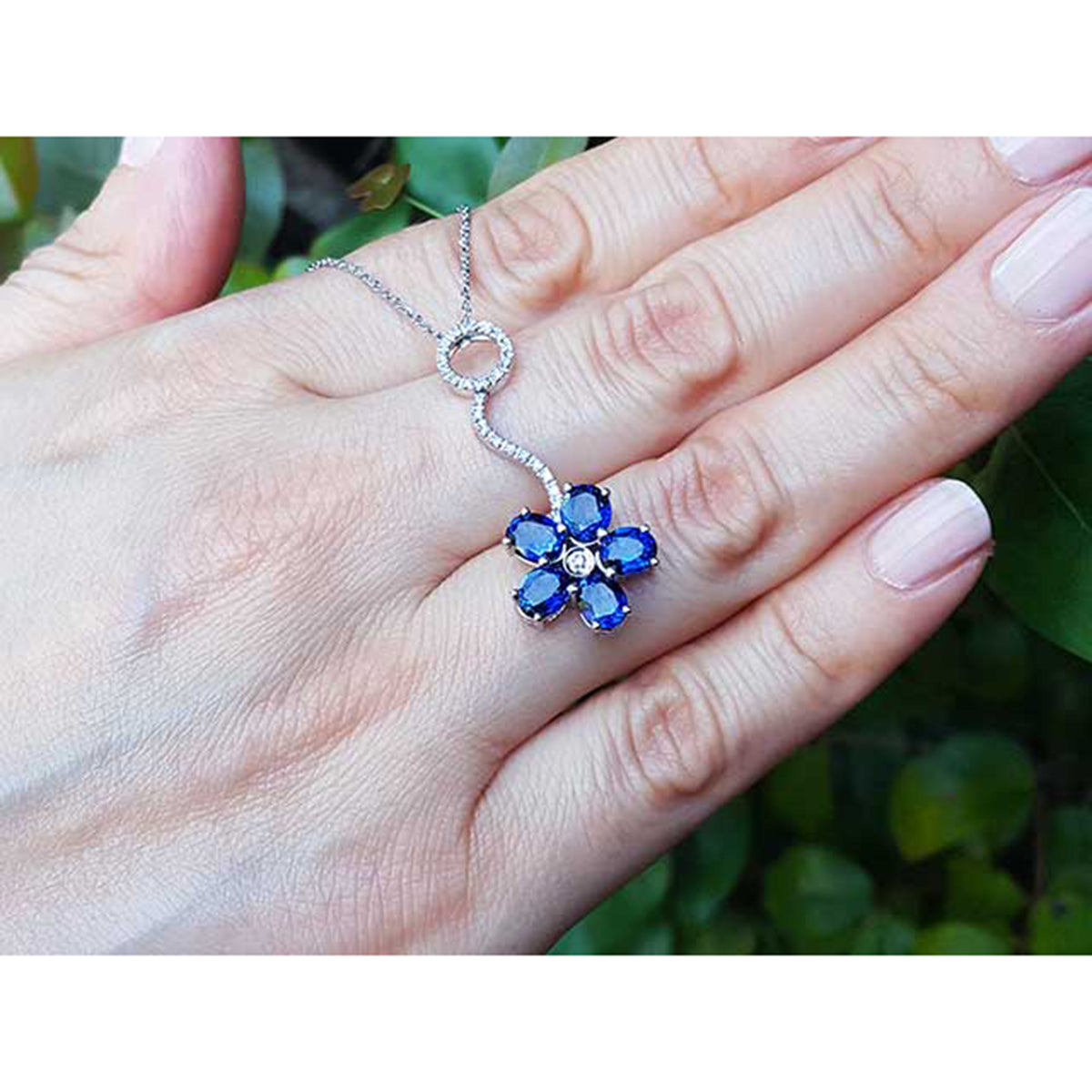 A cluster of natural sapphires pendant white gold necklace displayed on a person&#39;s hand