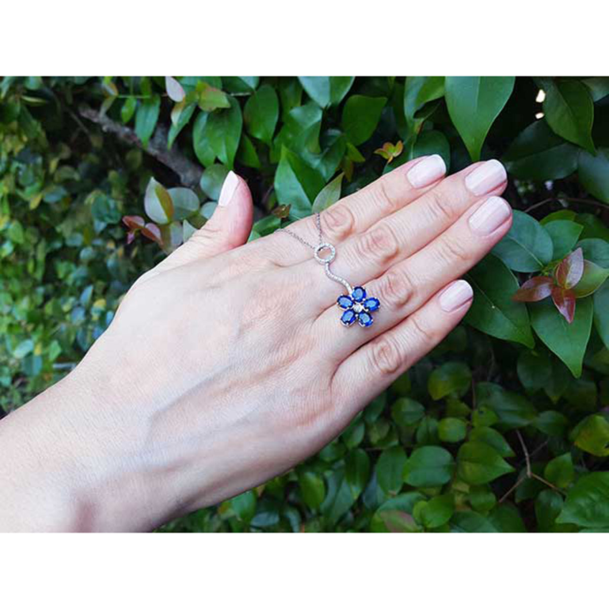 A woman&#39;s hand displaying a cluster of natural sapphires pendant white gold necklace on a leafy background
