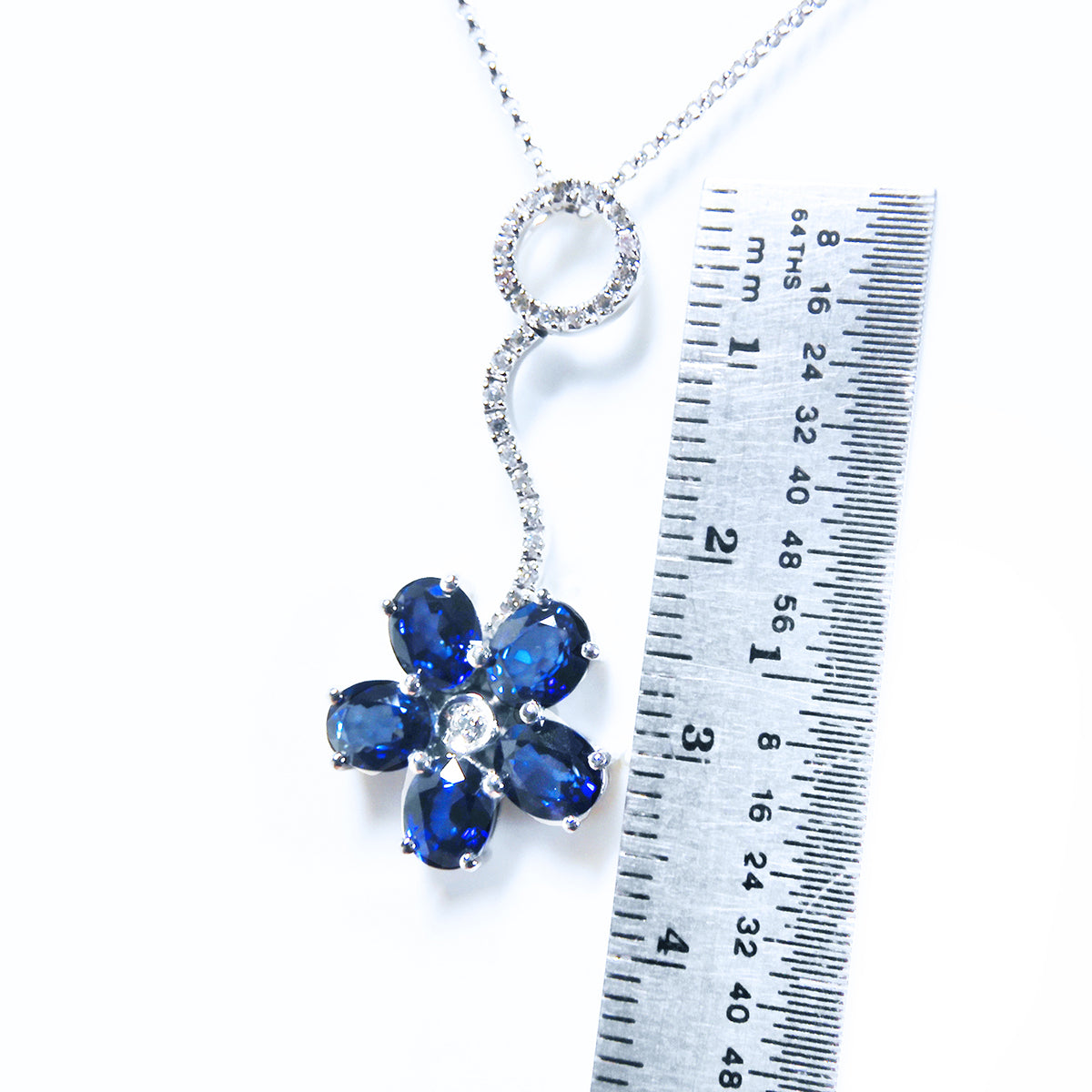 A cluster of natural sapphires pendant white gold necklace nest to a ruler for measure