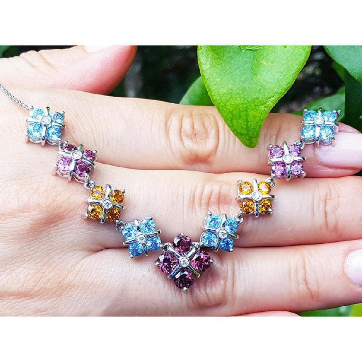 18K white gold X-cluster necklace with tri-colored topaz and diamond links on a hand.