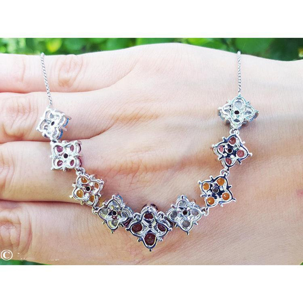 18K white gold X-cluster necklace with tri-colored round-cut natural topaz and diamond links on a hand.