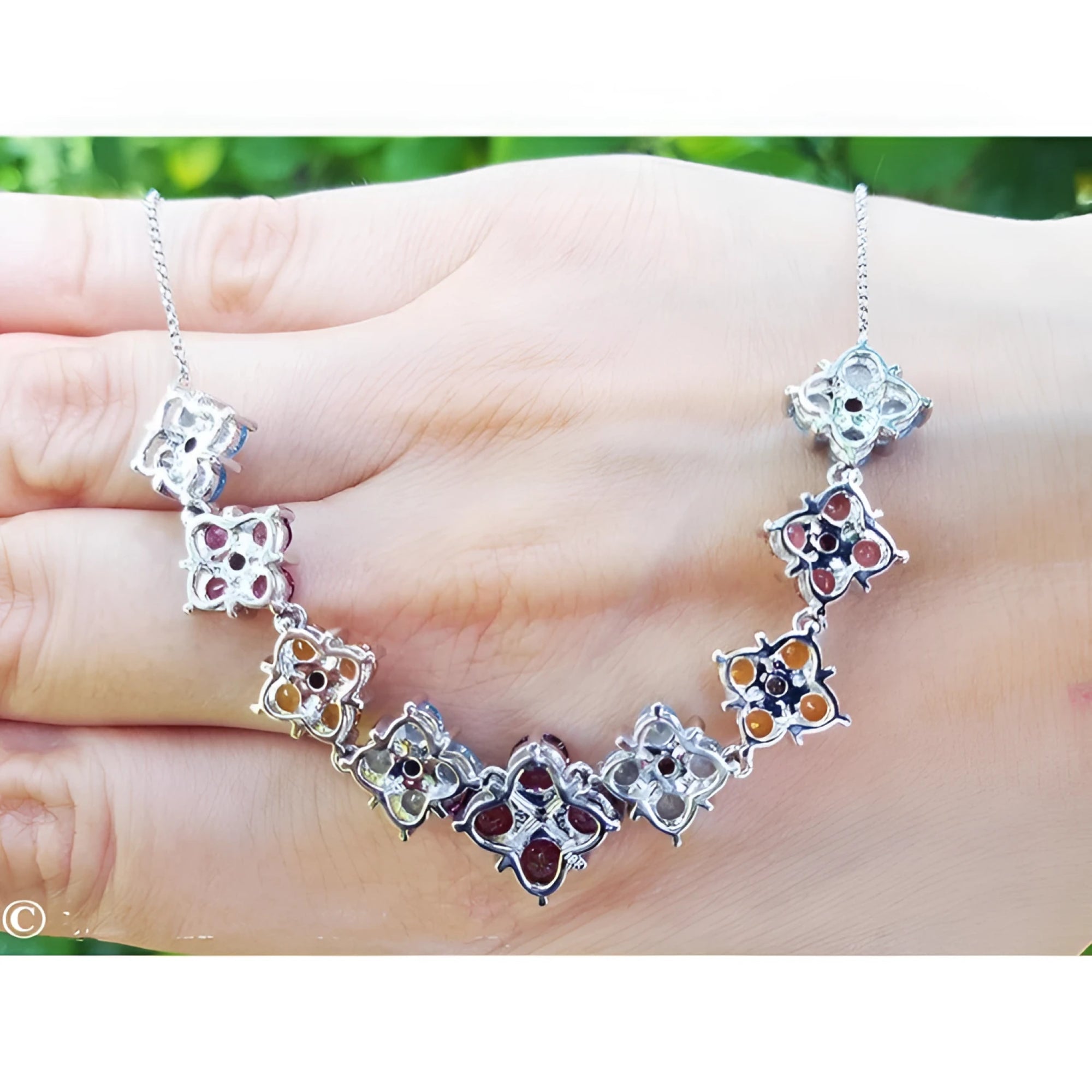 18K white gold X-cluster necklace with tri-colored round-cut natural topaz and diamond links on a hand.