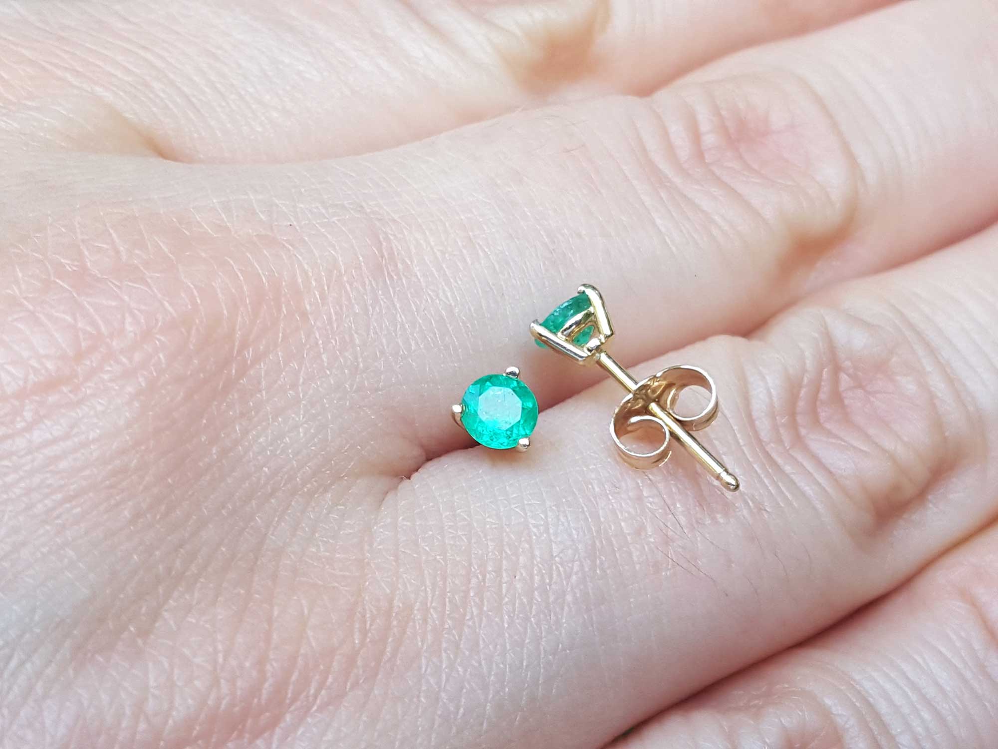 Hand displaying a pair of emerald cocktail earrings made in 14k yellow gold.