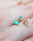 Hand displaying a pair of emerald cocktail earrings made in 14k yellow gold.