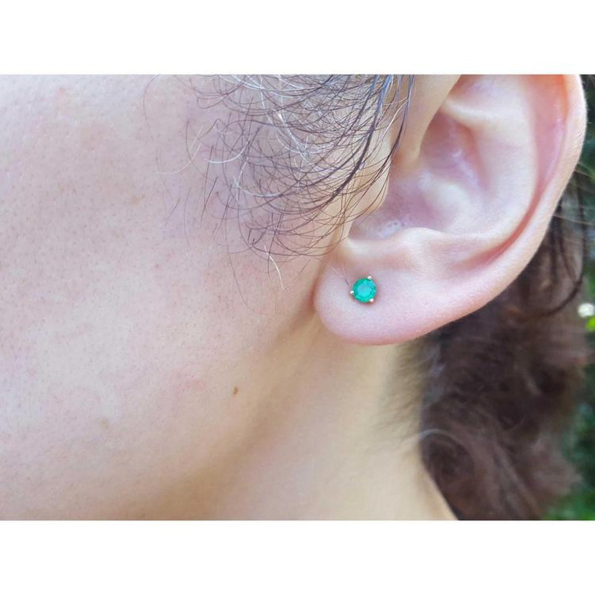 Cocktail emerald stud earring with a medium deep green gemstone in 14K yellow gold, worn on an ear.