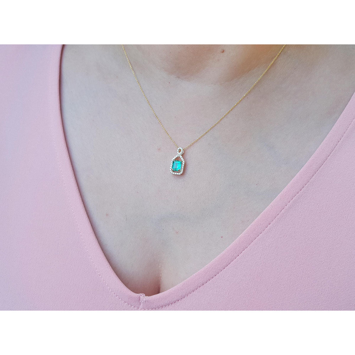 Women&#39;s emerald jewelry necklace square emerald-cut, halo diamond 14k yellow gold on a pink top.