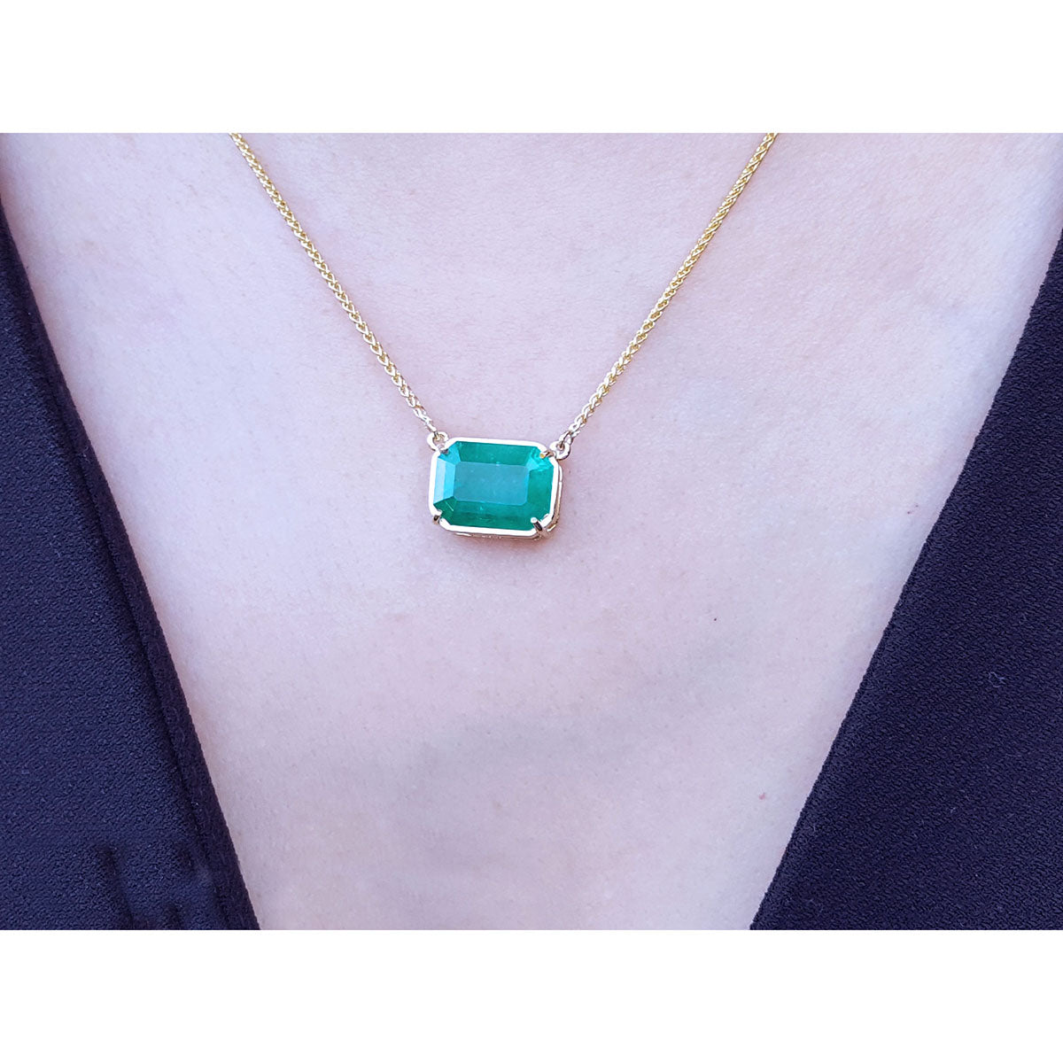 18k yellow gold necklace with a natural emerald pendant on a woman wearing a dark blue top.