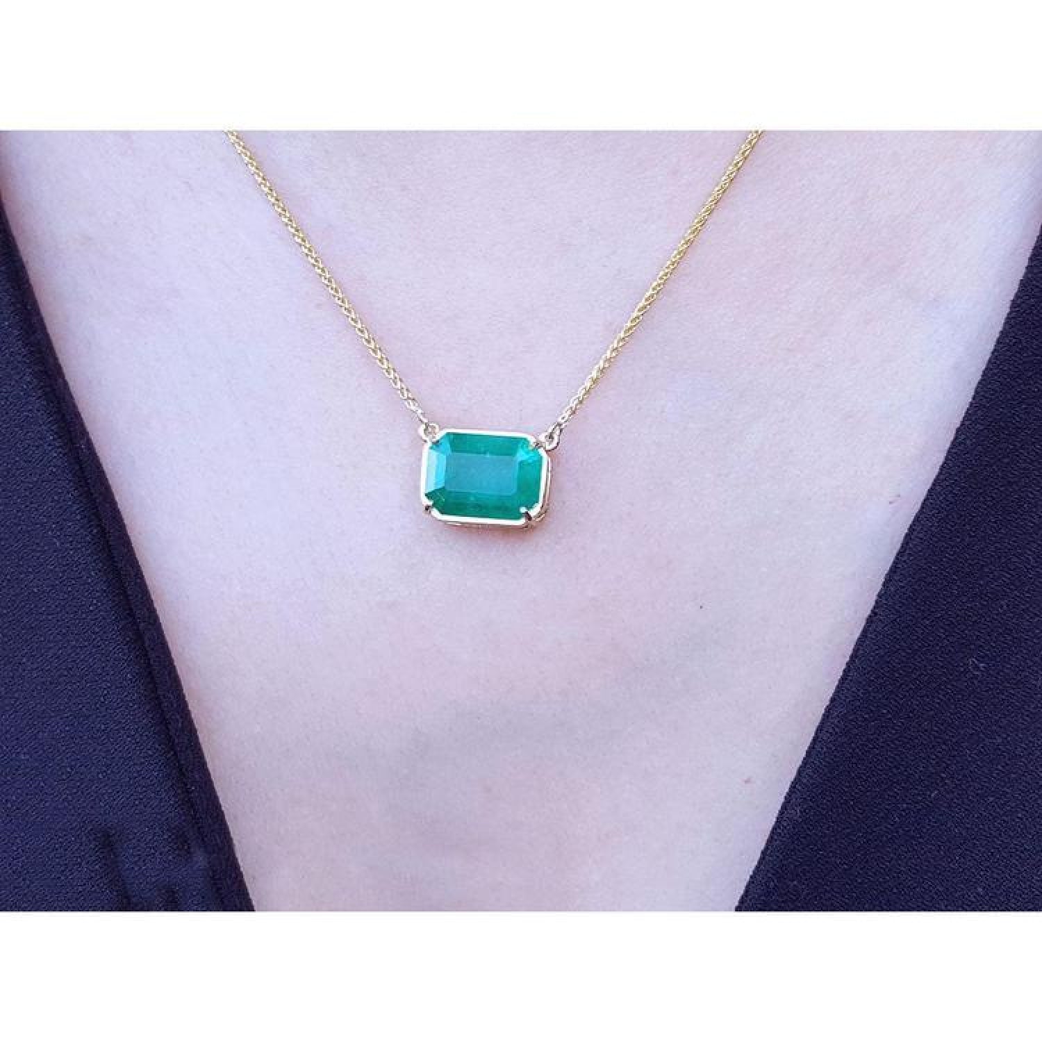 Emerald-cut Colombian emerald solitaire necklace in 18K yellow gold, on a black top, shown worn on a model's neck.