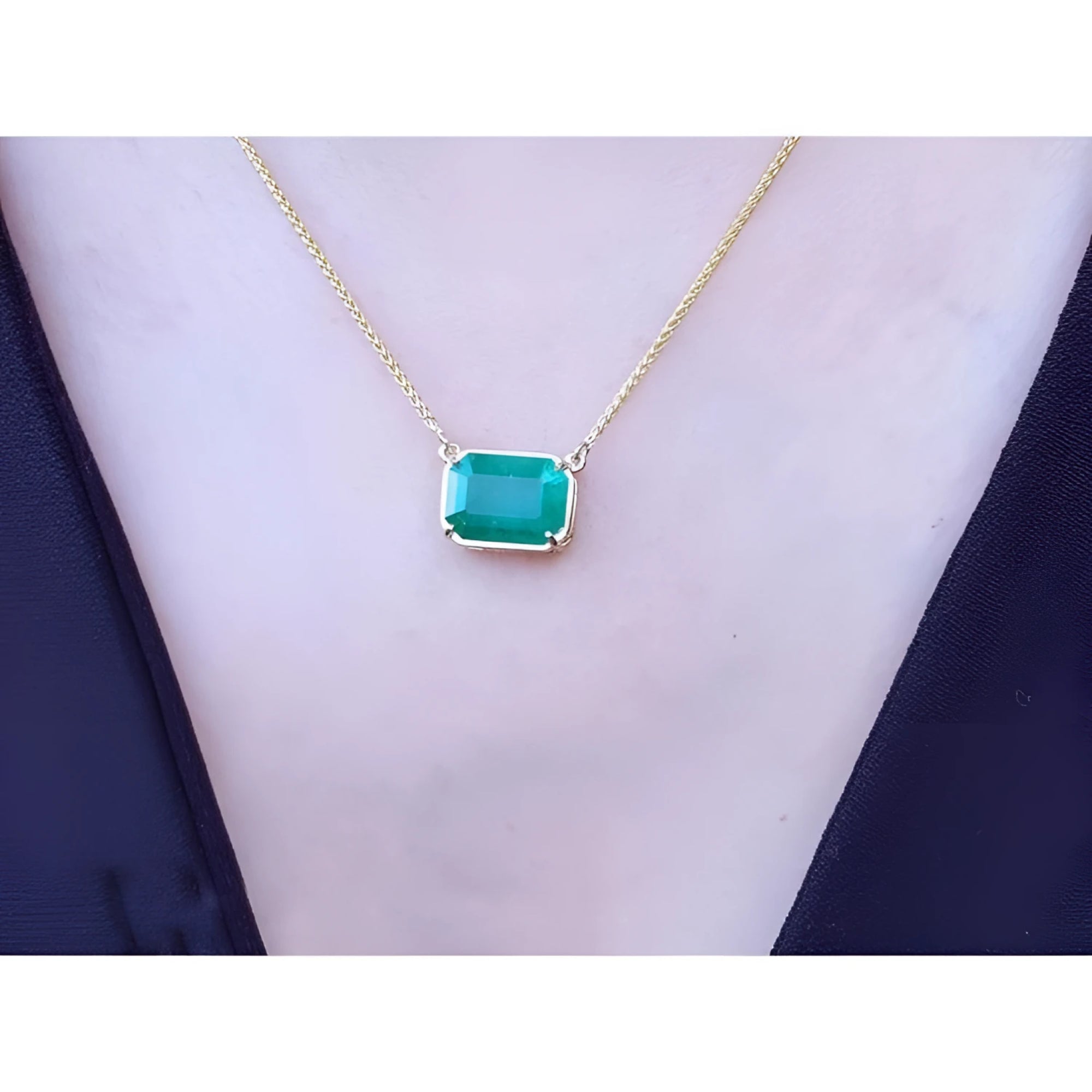 Emerald-cut Colombian emerald solitaire necklace in 18K yellow gold, worn on a black top.