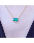 18k yellow gold necklace with a natural emerald pendant on a woman wearing a dark blue top.