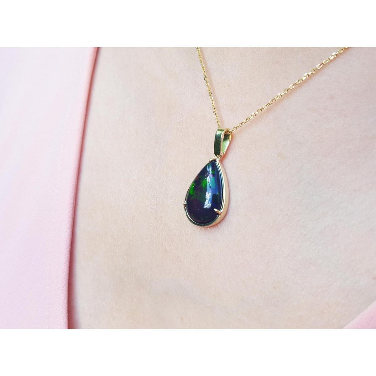 Teardrop-shaped Wello black opal pendant on a gold chain against a pink background
