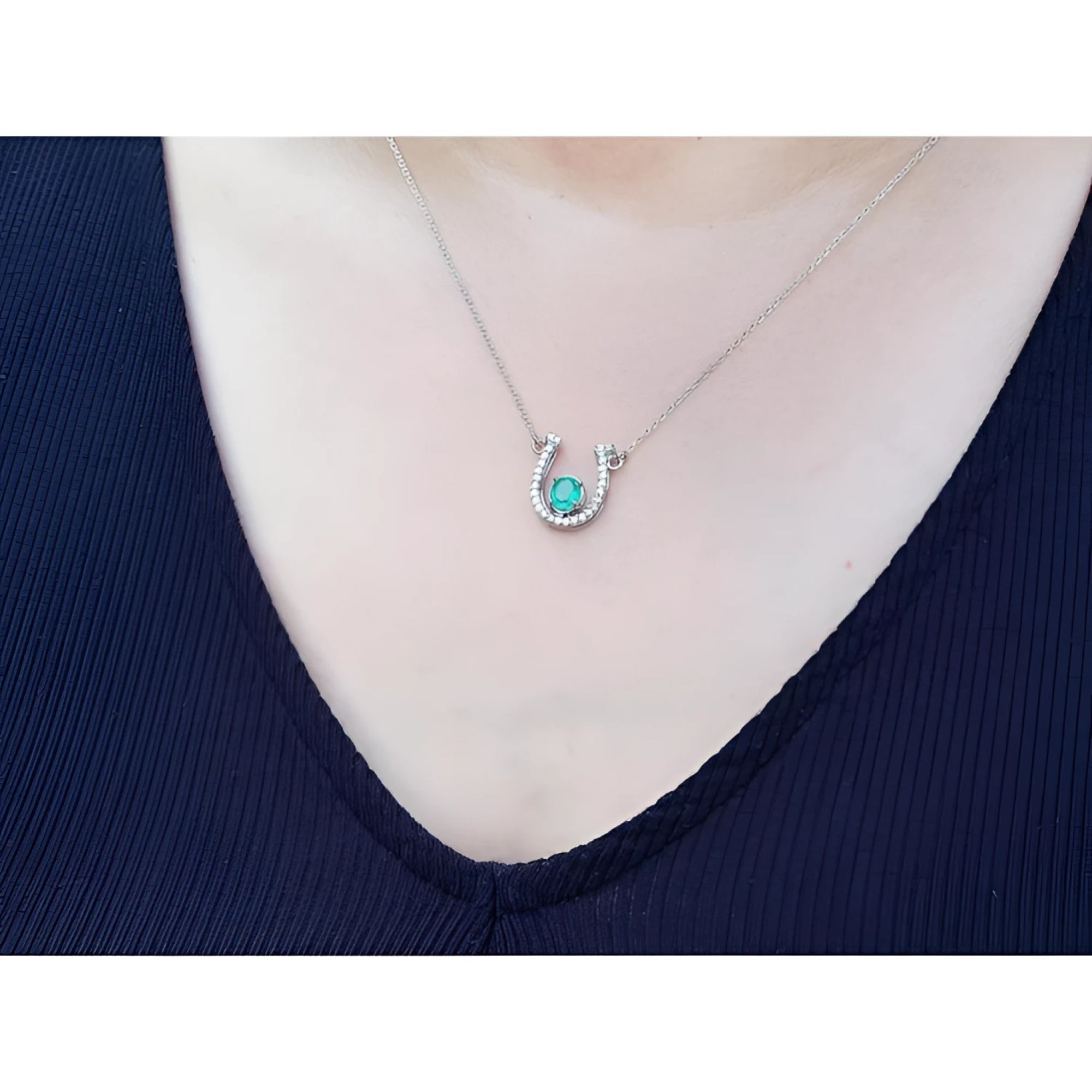 White gold oval emerald horseshoe necklace with diamonds, worn on a person.
