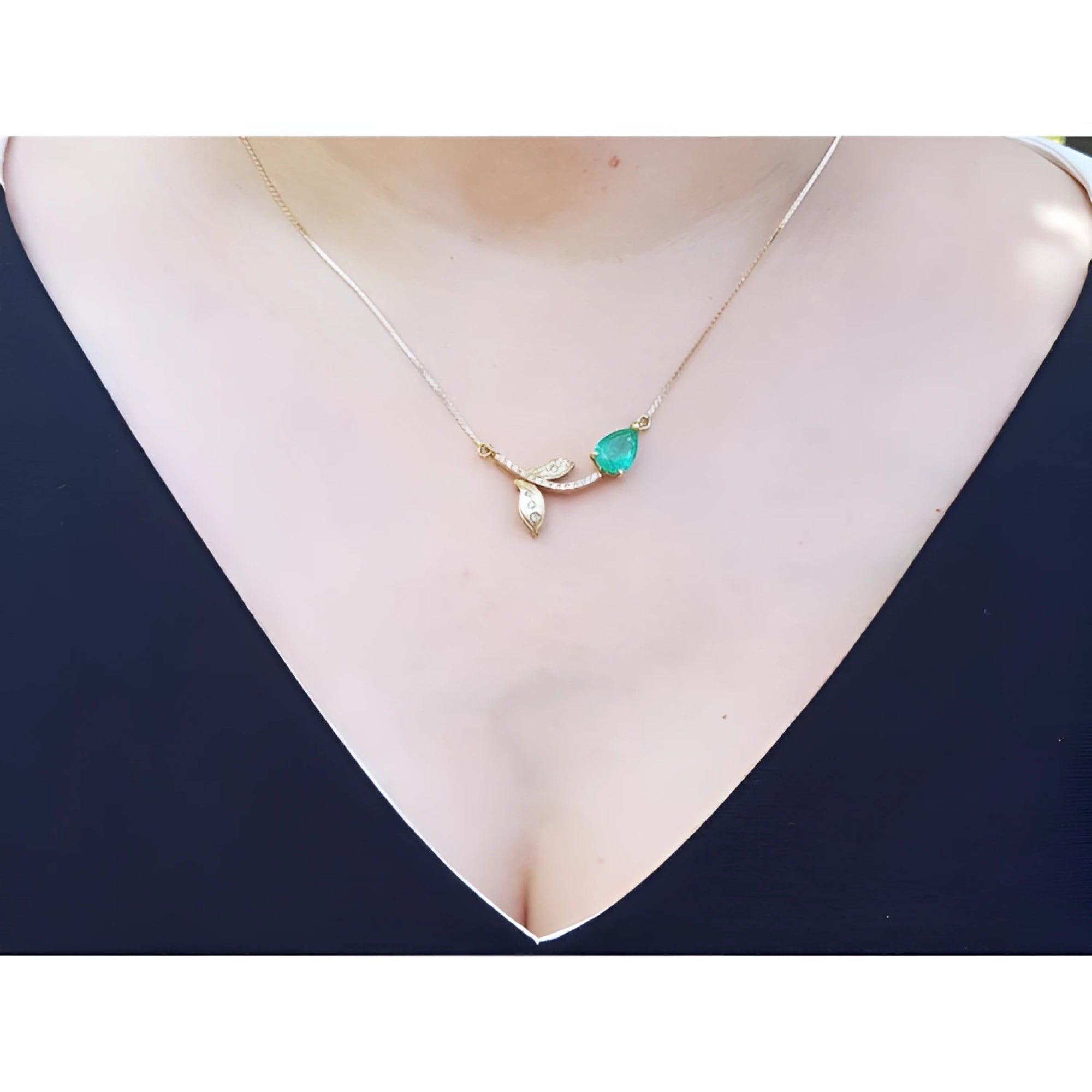 14K yellow gold twig necklace with a pear-cut natural emerald and diamond leaves on a woman's neck.
