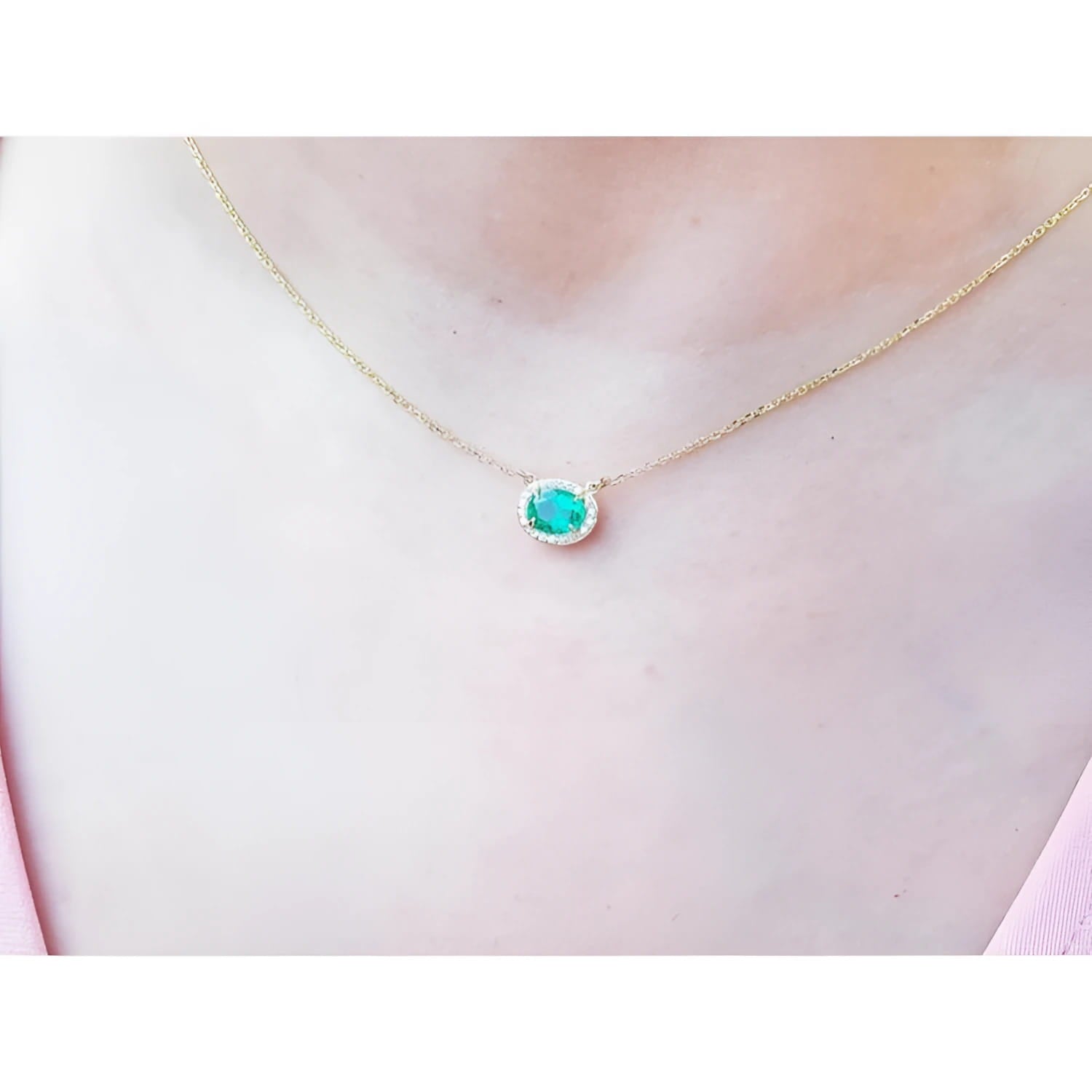 Oval Muzo emerald necklace with diamond halo on a delicate 14K yellow gold chain.