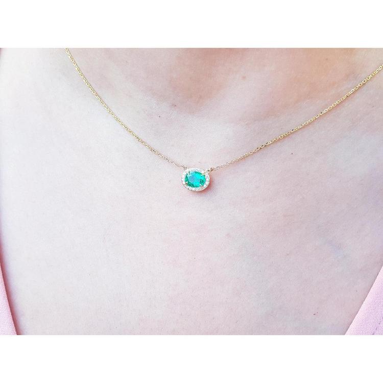 Oval Muzo emerald necklace with diamond halo on a delicate 14K yellow gold chain.