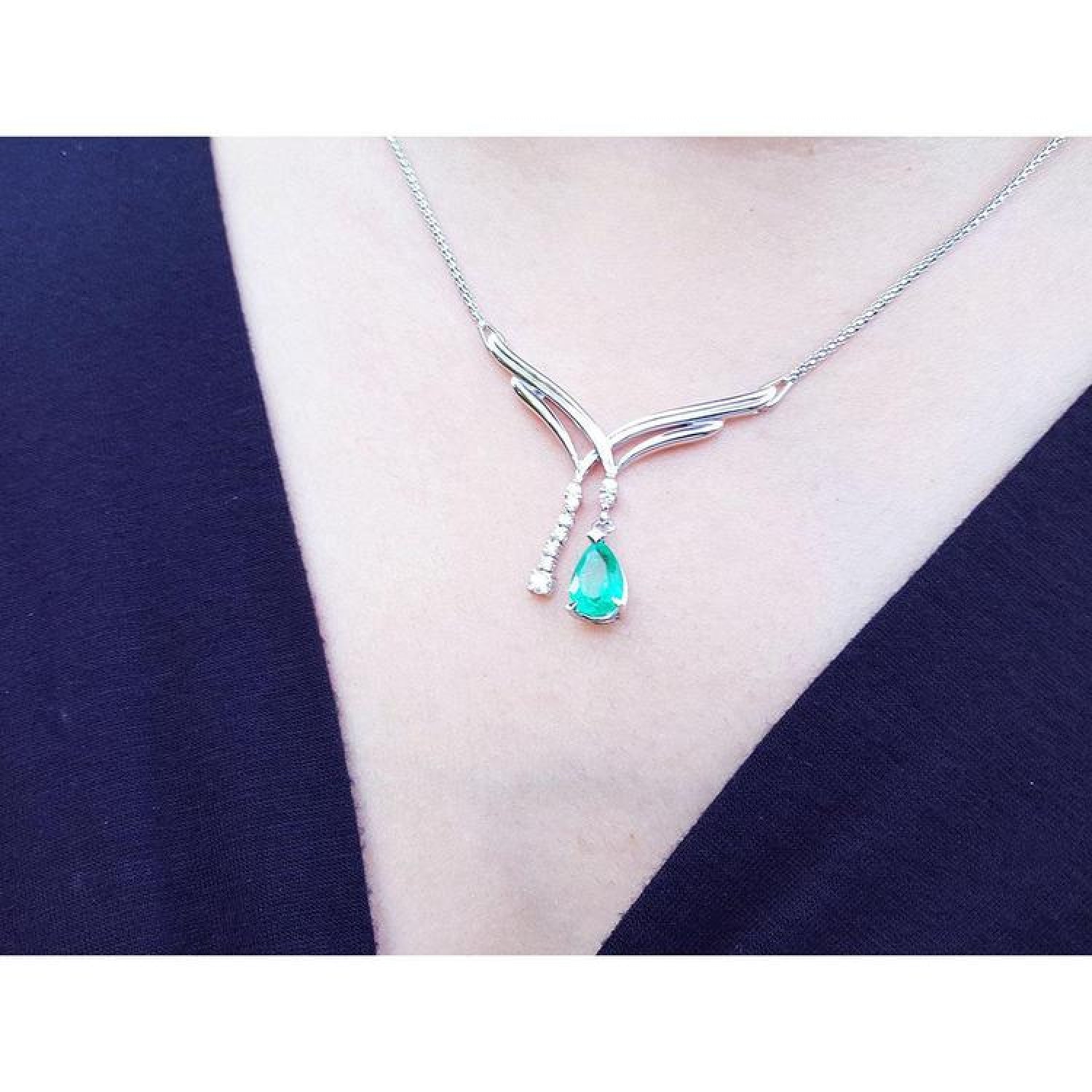 14K white gold necklace with a pear-shaped emerald and diamond chevron pendant on a woman's neck.