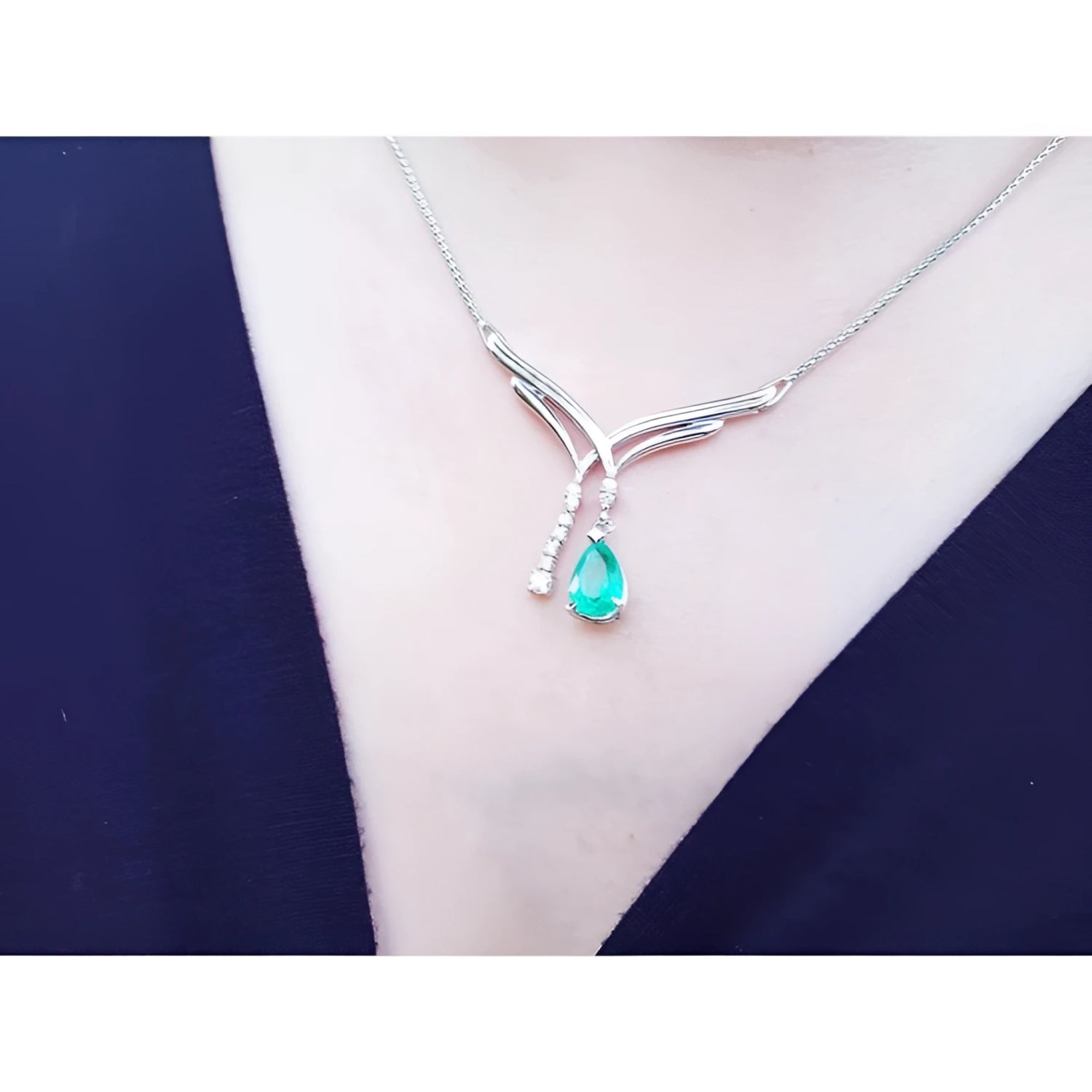 14K white gold necklace with a pear-shaped emerald and diamond chevron pendant on a woman's neck.