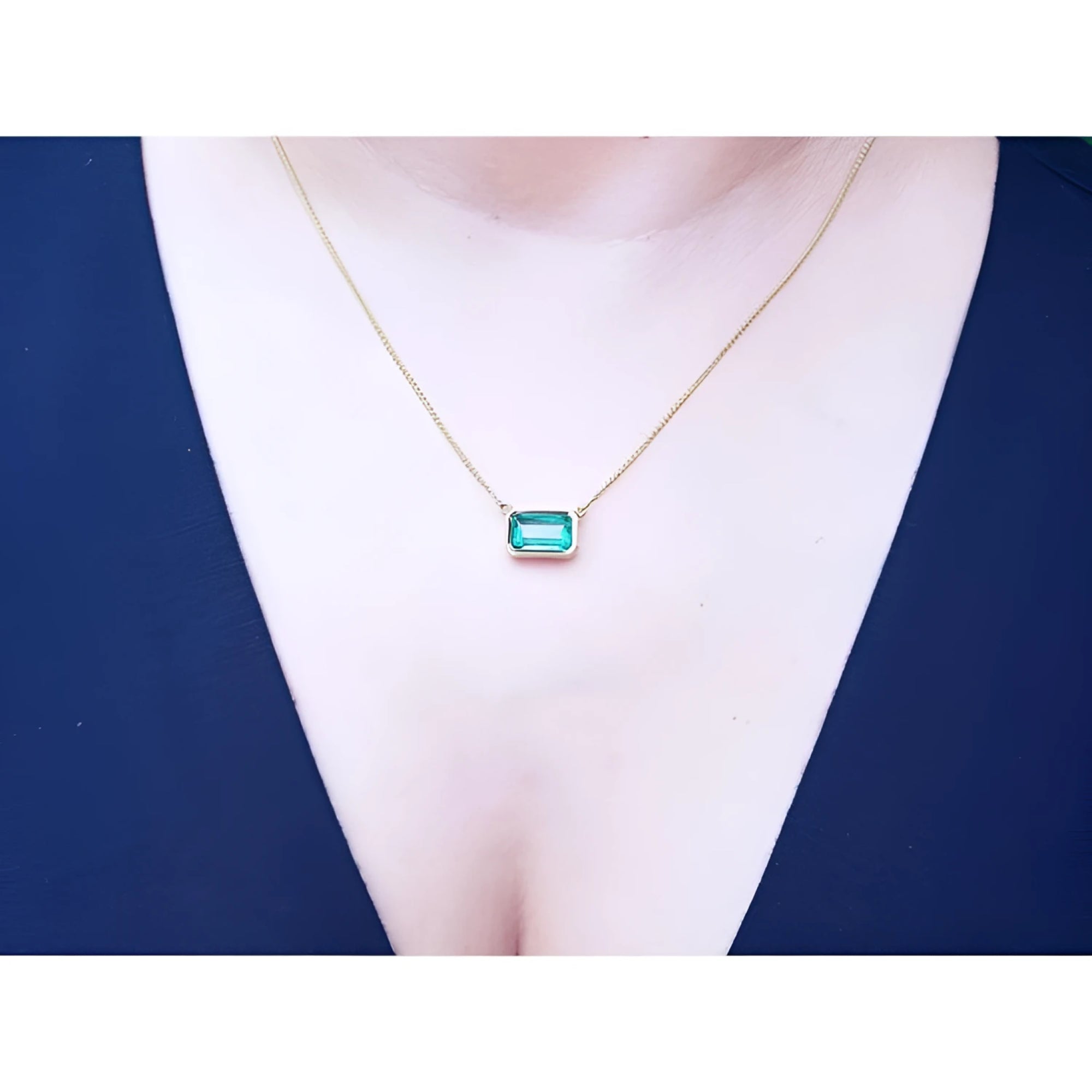 East-west rectangular emerald solitaire necklace in 18K yellow gold, worn on a person.