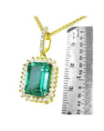 Emerald-cut emerald pendant with halo diamonds in 18K gold, shown next to a ruler for scale.