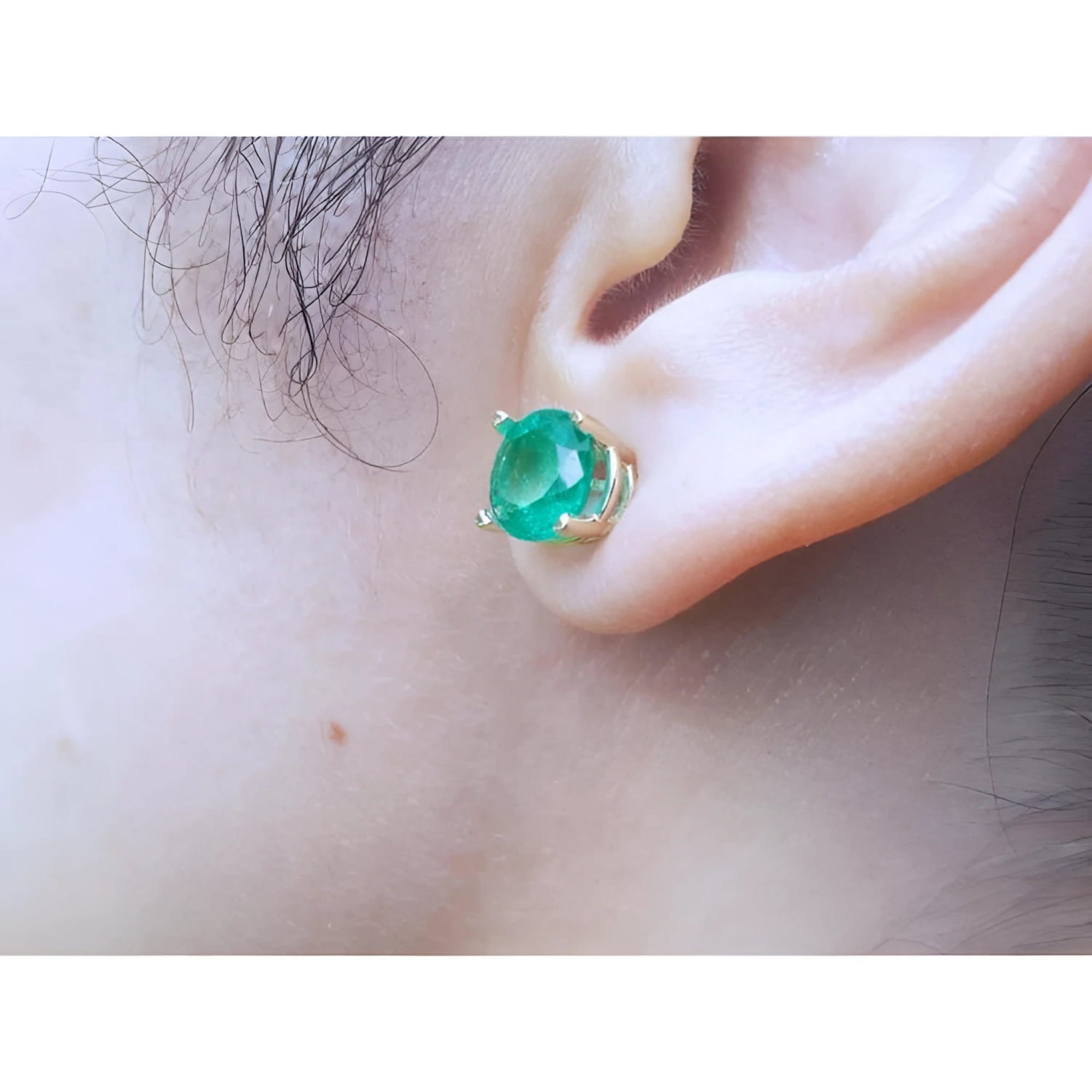 Round bluish-green Colombian emerald stud earring in 14K yellow gold prong setting on an ear.