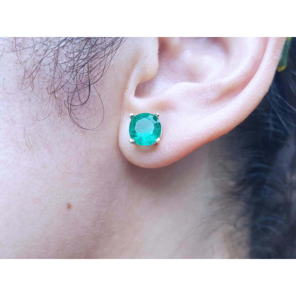 Close-up of an ear wearing a round cut emerald stud earring.