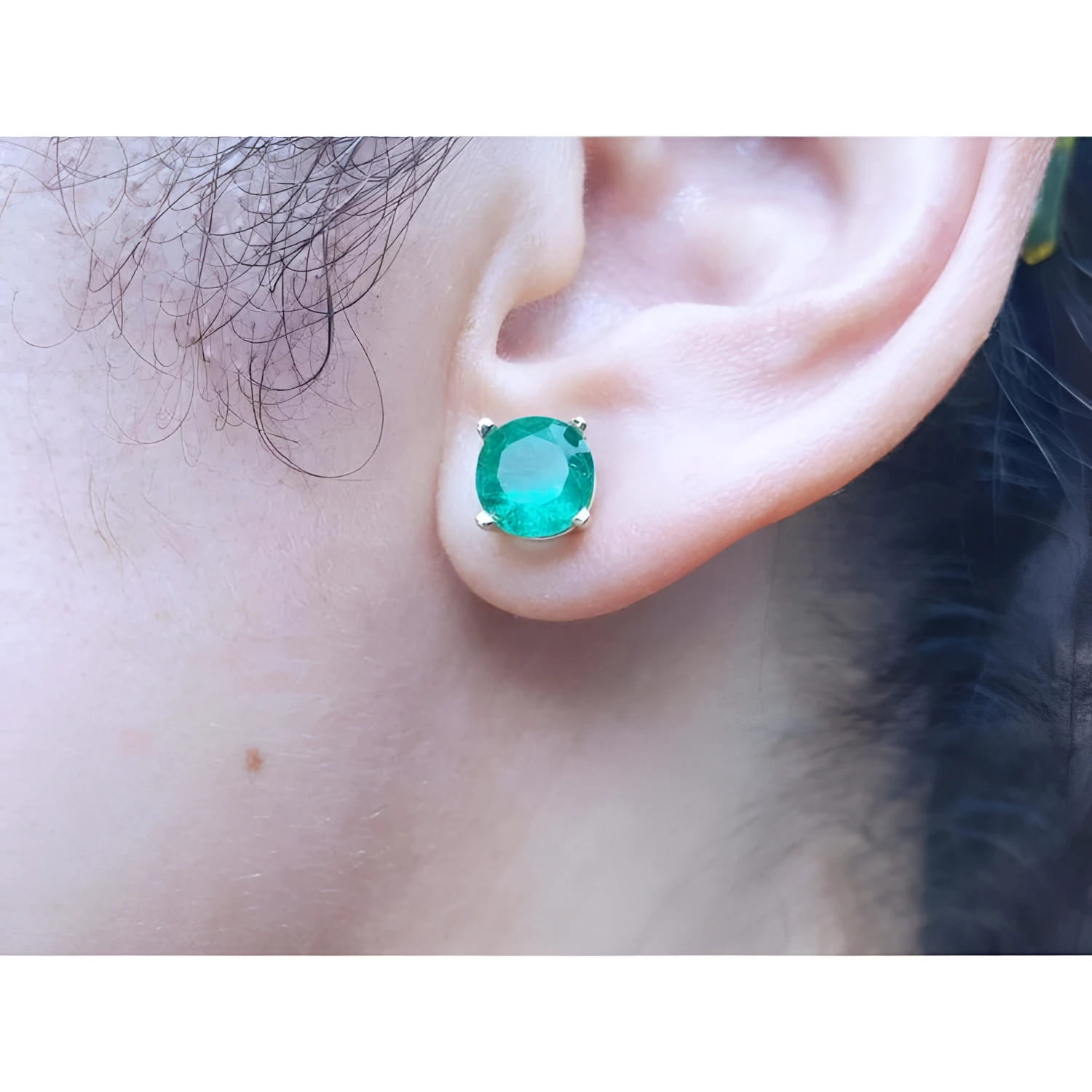 Close-up of an ear wearing a round cut colombian emerald stud earring.
