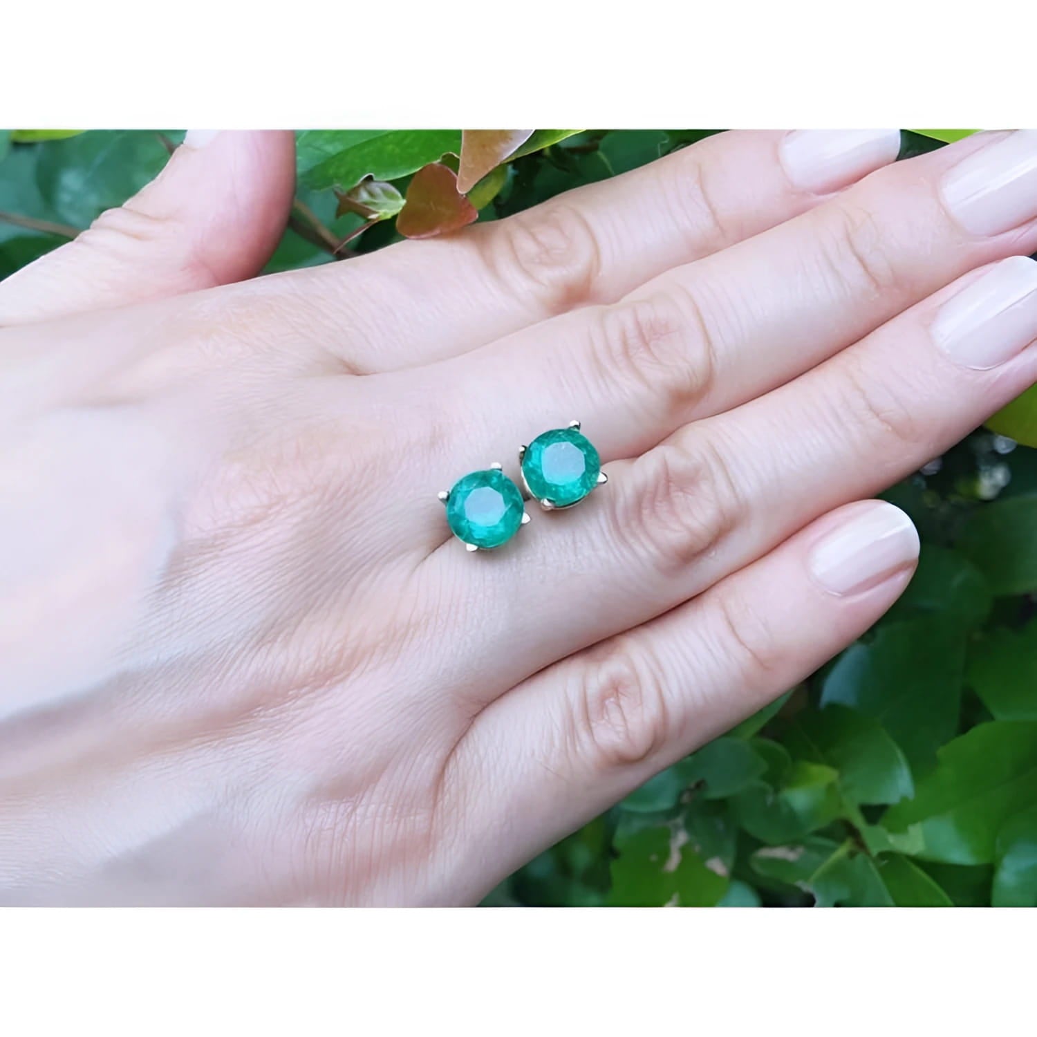 Round bluish-green Colombian emerald stud earrings in 14K yellow gold on a hand.