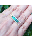 Emerald baguette cut necklace with natural diamonds, 14K yellow gold, and sliding tube bail chain. shown resting on a person's hand against a blurred green background.