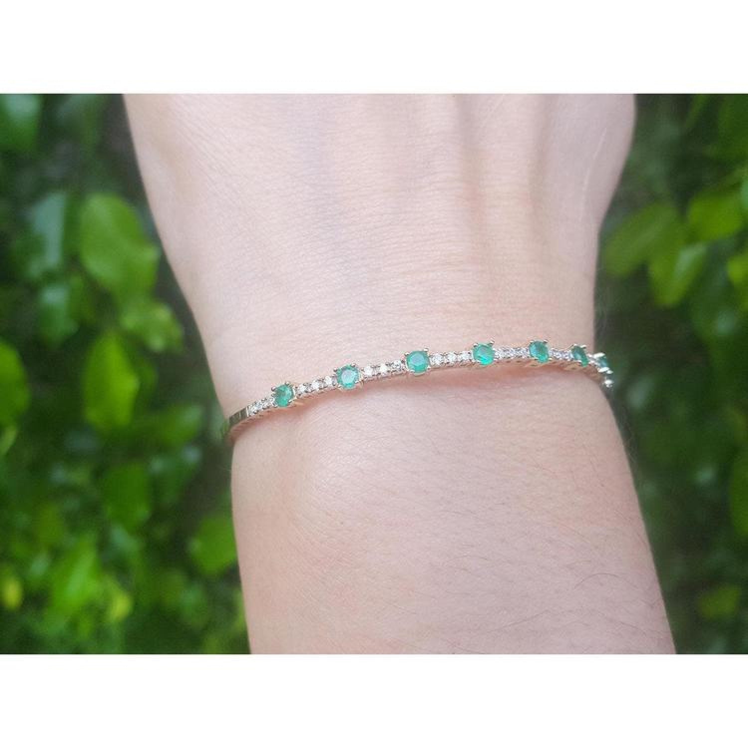 Flexible 14K yellow gold bangle with round emeralds and accent diamonds on a wrist.