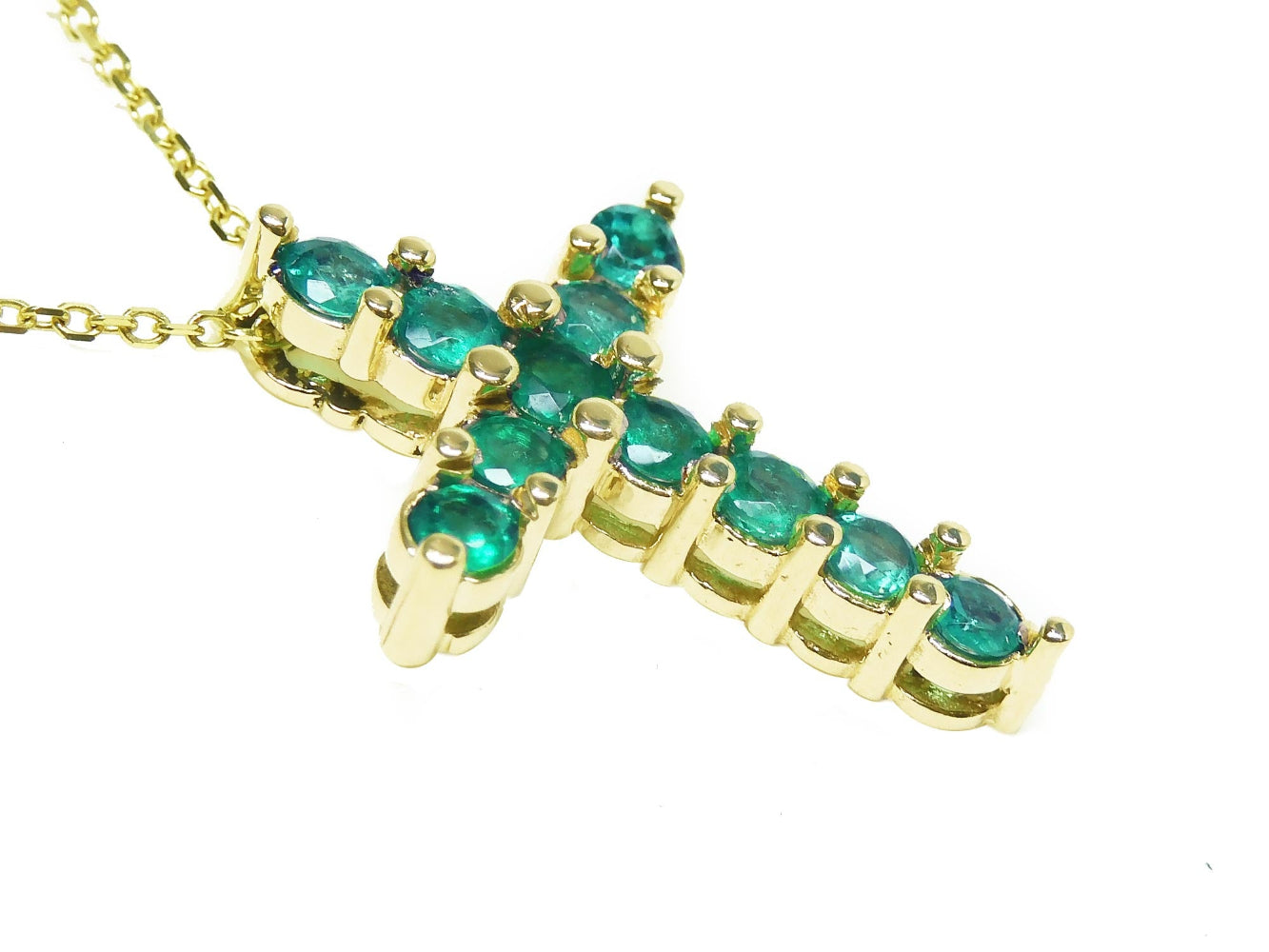A 14k yellow gold cross necklace pendant with natural colombian emeralds on a side profile view.