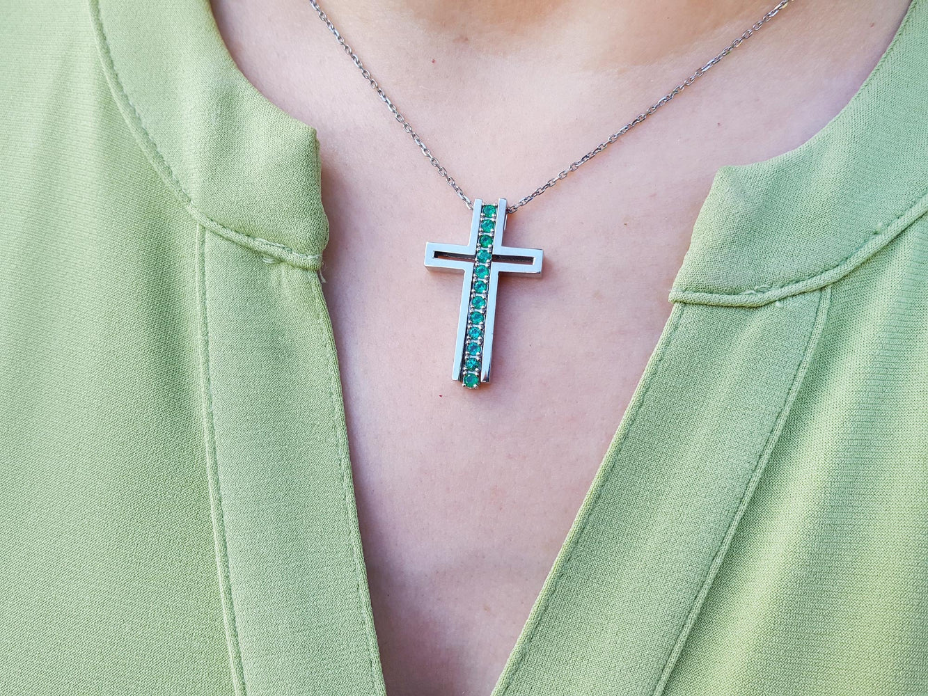 Cross-shaped necklace with genuine colombian emeralds worn by a person in a green top.