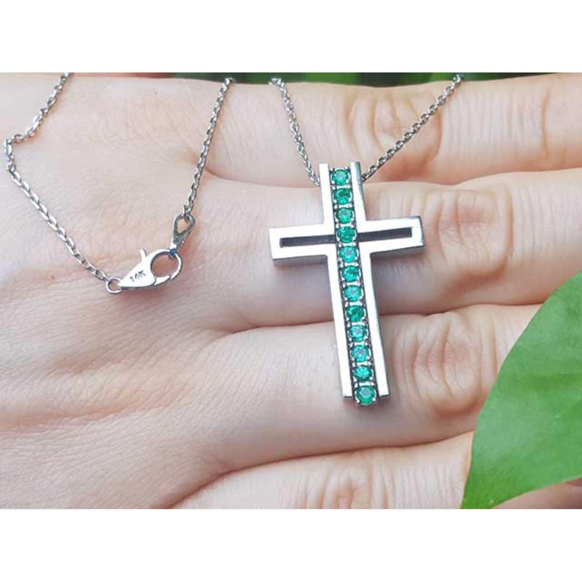 White gold cross pendant necklace with round emeralds held in a hand.
