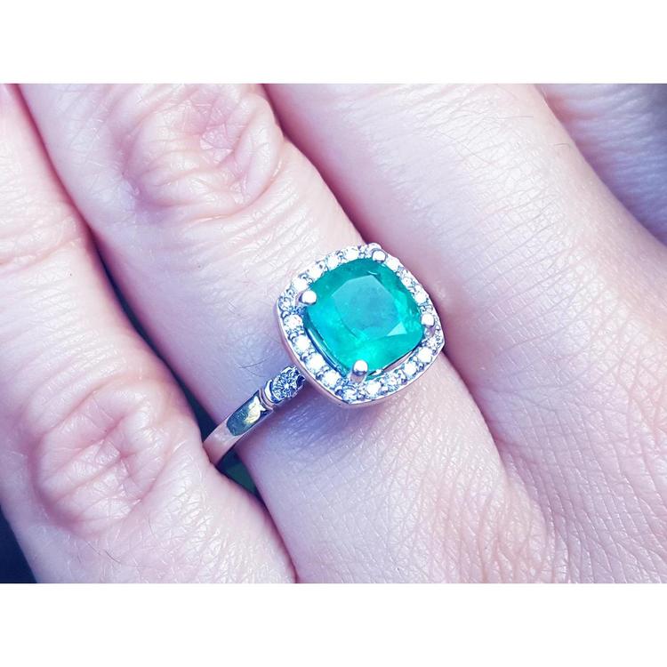 A natural Colombian emerald cushion cut with a halo diamond in white gold on a finger.